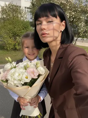 Снимок, сделанный на фронтальную камеру с низкой точки, запечатлел момент, наполненный жизнью и эстетикой. Яркие солнечные лучи освещают сцену, где девушка стоит рядом со школьным зданием. Ее лицо излучает радость, а волосы слегка развеваются на ветру. Она легко наклонила голову вбок, создавая непринужденный и естественный образ. На ней стильная одежда, которая подчеркивает ее индивидуальность, а на запястье переливается яркий браслет. Фон школы добавляет атмосферу дружелюбия и молодости, а общее настроение снимка вызывает чувство ностальгии и тепла.