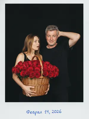 На черном фоне в стиле Polaroid, запечатленный на 35mm пленку в начале 2000-х, вспыхнувший свет. Мужчина и женщина, окруженные тьмой.

Женщина в черном топе, держа огромную корзину из плетеных нитей, наполненную красными розами. В ее глазах удивление, взгляд устремлен на мужчину.

Мужчина в свободной черной футболке, с легкой улыбкой, чешет голову, встречая прямой взгляд объектива.

Они просвечены ярким светом вспышки, камера фиксирует средний план. На белой рамке Polaroid, голубой ручкой, написано: «Февраль 14, 2026».

Аутентичное зерно пленки, высокий контраст, добавляющий нотку ностальгии.