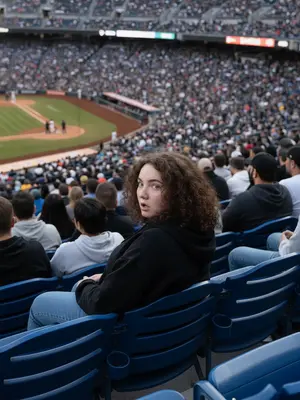 A figure in the stands at a major sports event, captured on a distant live broadcast camera. They are perched in a row of azure seats, reclining slightly, their gaze directed to the side in a moment of astonishment, lips subtly agape.
