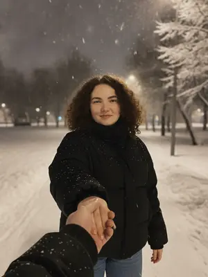 В заснеженном городском парке ночью происходит романтический и немного грустный момент. Девушка, одетая в объемную короткую черную куртку, стоит в центре кадра. Ее лицо ясно видно, и она держит парня за руку. Внезапно она поворачивается через плечо, улыбаясь мило и направляя свой взгляд прямо в камеру.

На переднем плане заметна рука парня, который делает снимок. Их пальцы переплетены, создавая классическую картину "следуй за мной" и подчеркивая близость пары. Рука парня укутана в черную куртку с нарядными манжетами.

Окружающая обстановка наполнена зимней эстетикой. Справа от них стоят деревья, покрытые густым слоем снега, и уличные фонари, излучающие мягкий и теплый свет. В воздухе парят крупные хлопья падающего снега, создавая ощущение движения и глубины кадра.

Эта фотография захватывает момент прогулки, наполненный движением, ветром и эмоциональной близостью. Она кажется кадром из жизни, извлеченным из блога о стиле жизни или короткого видео для социальных сетей, где романтический настрой создает интригу и ощущение неожиданного поворота.