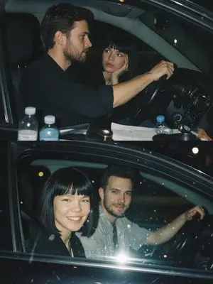 Создайте коллаж из двух фотографий, расположенных одна под другой. На верхней фотографии - ночной снимок в салоне автомобиля: мужчина за рулем сосредоточенно смотрит вперед, на его руке видны часы. Женщина, находящаяся на пассажирском сиденье, внимательно слушает его, подперев щеку рукой. Этот кадр выполнен в стиле папарацци с эффектом зернистой пленки, создавая интимную атмосферу.

На нижней фотографии - близкий план двух главных героев: мужчина за рулем и женщина на пассажирском сиденье обращены к камере. Женщина улыбается с ухмылкой, ее губы украшены бантиком, в то время как мужчина слегка улыбается, положив руку на руль. Этот кадр снят через пассажирское окно, сочетая ночной свет с вспышкой и добавляя эффект зернистой пленки для более выразительного визуального впечатления.
