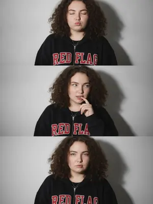 Представь себе трехкадровый вертикальный коллаж, где запечатлены разные эмоции одной женщины. В первом кадре она закрыла глаза и слегка придвинула губы вперед. На втором кадре ее лицо выражает игривую дерзость: она слегка скривила нос и закусила палец, взгляд бросила в сторону. На третьем кадре женщина смотрит прямо в объектив, через локоны волос, приоткрыв рот. На ее шее сверкает изящное серебряное ожерелье с кулоном. 

Женщина одета в огромное черное худи с красным принтом RED FLAG, который выделяется на фоне минималистичной белой стены. Освещение жесткое и резкое, создающее четкие тени от модели на стене, в стиле ночных фотосессий и Y2K эстетики. Фотография сделана на iPhone 17, обработана с натуральным внешним видом, без излишней ретуши, с легким цифровым шумом и нежной зернистостью.