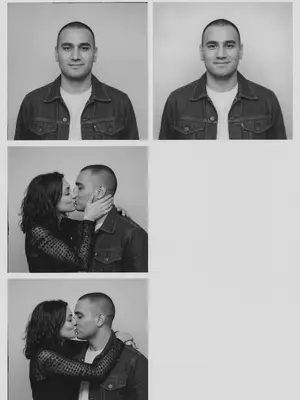 In a vintage black-and-white photobooth strip, a man and a woman are captured in four frames. The man dons a dark denim jacket over a light T-shirt, while the woman wears a fitted semi-sheer black long-sleeve top with delicate patterns. The energy between them is candid and authentic, with a natural, imperfect pose that feels unpolished and asymmetrical. The frames are stacked in a single column, each one showcasing a different moment. The background is a simple light studio setting, with white borders and square corners, evoking a realistic analog photobooth vibe.

In the first frame, they stand side by side facing the camera, the woman on the left and the man on the right. The woman's head is slightly turned to the right, with a flirtatious smile and a sidelong glance, creating a symmetrical yet slightly off-center composition. Moving to the second frame, the woman turns towards the man, gently cupping his cheek with a bright smile, while he looks back at her with a soft expression. Their closeness creates a left-weighted composition with empty space on the right.

In the third frame, the couple shares a kiss in profile, the woman on the left and the man on the right, positioned towards the left side of the frame with extra space on the right. Her hand rests on his cheek as they embrace. Finally, in the fourth frame, the woman hugs the man from behind over his shoulders, leaning her head towards him from the upper left corner, while he smiles at the camera. The couple is close to the left side of the frame, leaving the right half empty for a balanced yet intimate composition.