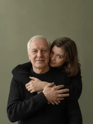 На студийском фотосете запечатлен отец и его дочь, обнимающиеся. Девушка стоит позади мужчины, ее руки ласково обвивают его торс, щека едва касается его головы. Взгляд обоих направлен точно в объектив. В их выражениях - спокойствие, теплота и натуральная нежность, с легкой улыбкой на лицах. 