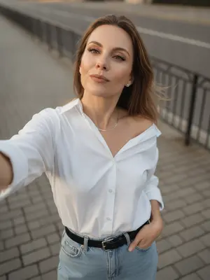 Изображение сделано на фронтальную камеру смартфона, который держится на вытянутой руке. Ракурс позволяет видеть сцену сверху вниз, создавая крупный план. Одна рука спокойно опущена вдоль тела, в то время как другая рука вытянута вперед для селфи. 