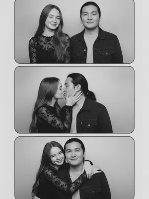 In a vintage black-and-white photobooth strip, a man and a woman are captured in four frames. The man dons a dark denim jacket over a light T-shirt, while the woman wears a fitted semi-sheer black long-sleeve top with delicate patterns. The energy between them is candid and authentic, with a natural, imperfect pose that feels unpolished and asymmetrical. The frames are stacked in a single column, each one showcasing a different moment. The background is a simple light studio setting, with white borders and square corners, evoking a realistic analog photobooth vibe.

In the first frame, they stand side by side facing the camera, the woman on the left and the man on the right. The woman's head is slightly turned to the right, with a flirtatious smile and a sidelong glance, creating a symmetrical yet slightly off-center composition. Moving to the second frame, the woman turns towards the man, gently cupping his cheek with a bright smile, while he looks back at her with a soft expression. Their closeness creates a left-weighted composition with empty space on the right.

In the third frame, the couple shares a kiss in profile, the woman on the left and the man on the right, positioned towards the left side of the frame with extra space on the right. Her hand rests on his cheek as they embrace. Finally, in the fourth frame, the woman hugs the man from behind over his shoulders, leaning her head towards him from the upper left corner, while he smiles at the camera. The couple is close to the left side of the frame, leaving the right half empty for a balanced yet intimate composition. 