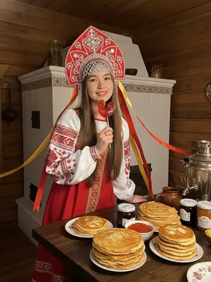 Изображение женщины в традиционном русском костюме Масленицы. На ее голове великолепный кокошник ярко-красного цвета, украшенный бриллиантами, стразами и длинными лентами, которые волнуются по сторонам. 