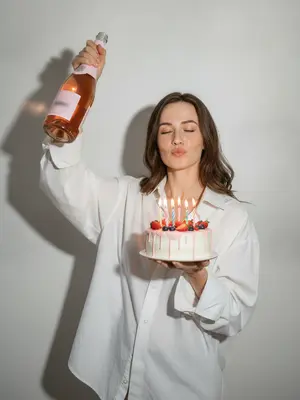 Изображение в стиле Party Girl / Birthday Aesthetic, сделанное в ультрареалистичной манере, как будто случайный снимок на старую цифровую камеру. Девушка в свободной белой рубашке оверсайз, застегнутой на пуговицы. В ее одной руке бутылка розового шампанского, которую она держит высоко, а другая рука держит небольшой бенто-торт с яркими свечами и свежими ягодами. 