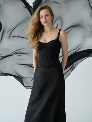 На студийном снимке fashion-портрета ультрареалистичного стиля, крупный план модели от груди до бедер. Модель стоит на белой циклораме, окруженной чистотой. За ней расправлена ткань из черного шифона, плавно колышущаяся под воздействием ветра. Этот элемент создает драматический фон с графичными контурами, ярко выделяясь на фоне белого пространства студии. 