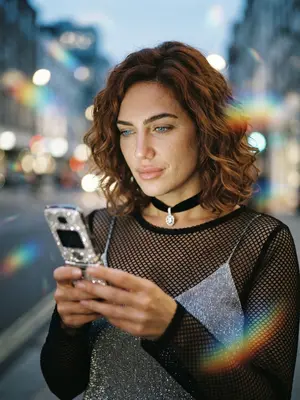 Создание эффектного портрета в стиле Y2K с использованием искусственного интеллекта. Изображение включает в себя раскладушку, украшенную стразами, блестящий чокер и радужные отблески. Освещение вечернее, создающее мечтательный эффект размытости. Выбор прически и возможность внести изменения во внешность, такие как цвет волос или фигура, доступны по желанию. 
