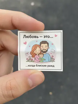 Фотография сделана крупным планом, под естественным светом. В кадре видна рука, которая держит маленький бумажный вкладыш, похожий на тот, что обычно встречается в упаковке жевательной резинки. На нем изображен рисунок, который немного помят. Основное внимание уделено именно этому вкладышу. 